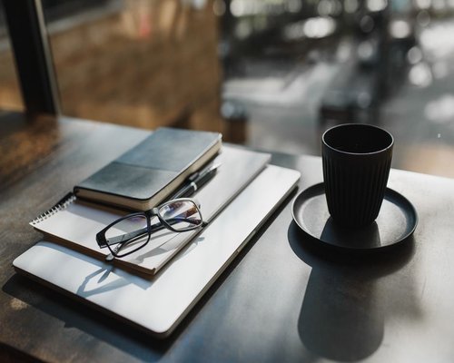 A cup of coffee and glasses on a desk with natural light